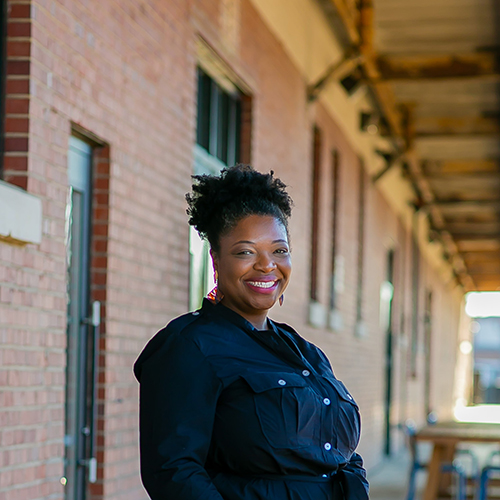 Smiling African American female standing outside of a brick building. 