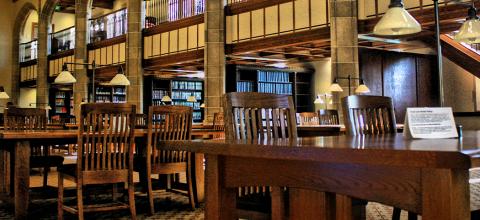 Library at a law school with brown wooden chairs and tables in front of rows of bookshelves.