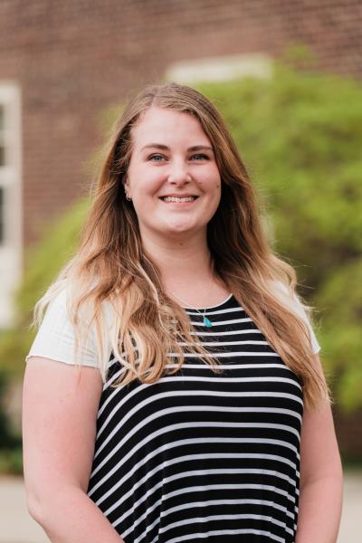 Ali Rill, a white woman with blonde hair, smiling and standing outside Grange building