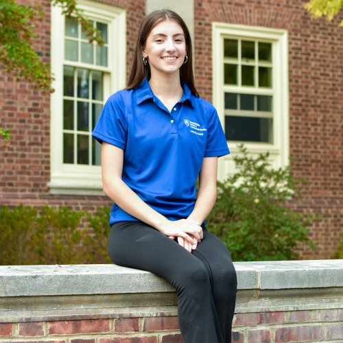 DUS Leadership Council member Addy sitting on a concrete wall outside Grange Building.