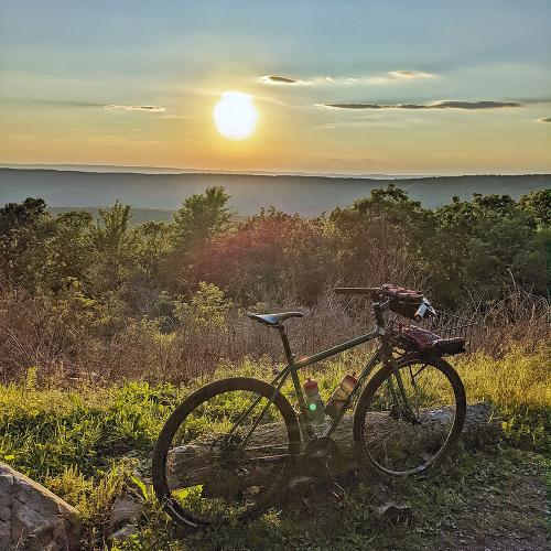 Bike on wooded summit, mountains and sunset in distance