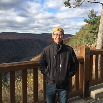Asian male standing on a wooden deck overlooking mountains in the fall. 