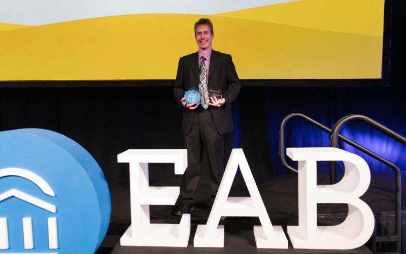 John Ellenberger posing on stage holding awards 