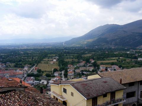 VIew above Italian town showing stone buildings with ceramic tile roofs and mountainsin the distance. 